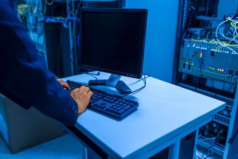 Un profesional de TI maneja un ordenador en una sala de servidores, gestionando sistemas de red y dispositivos conectados.